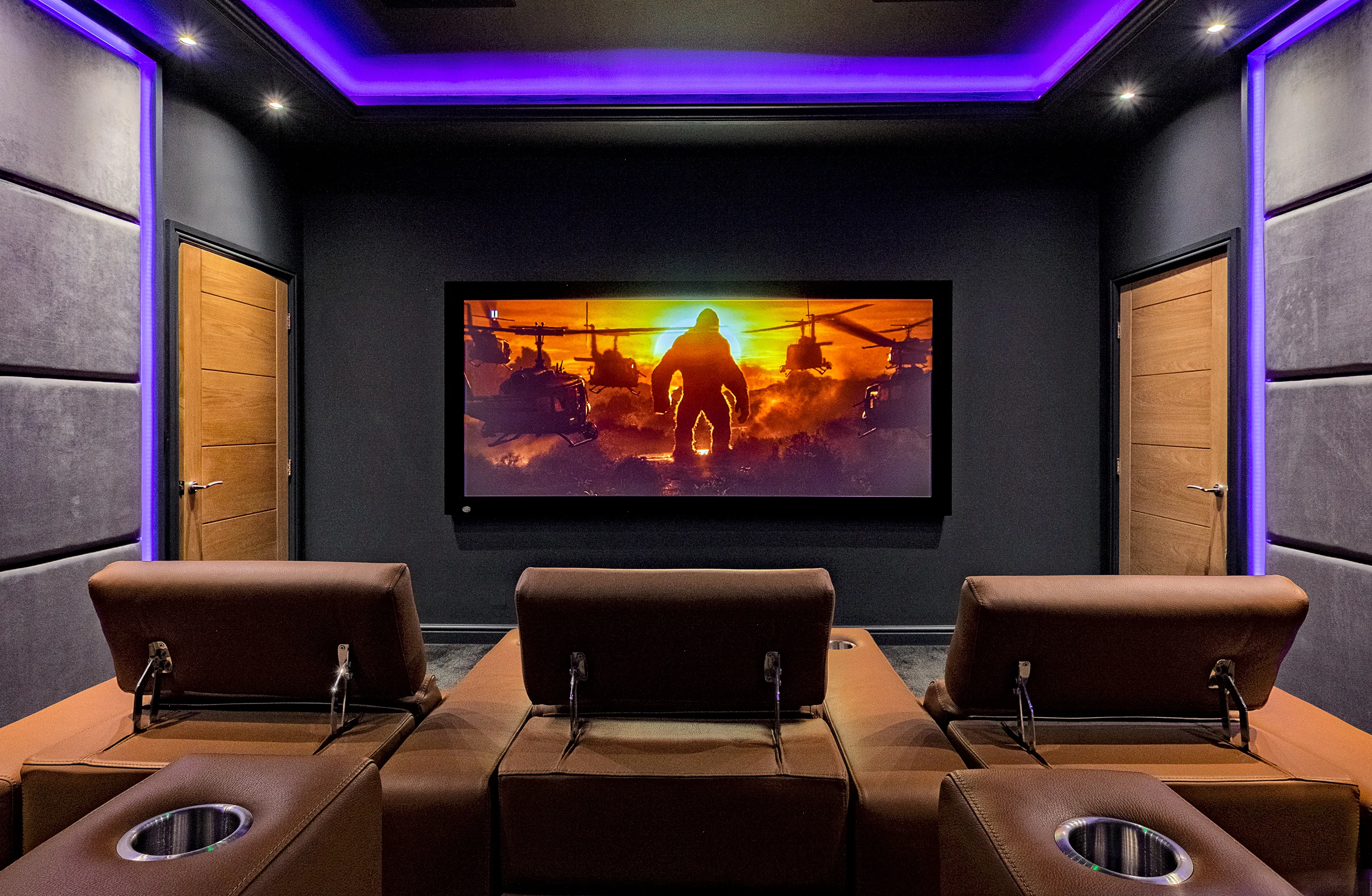 A dedicated home cinema room with a wide screen, leather recliners and purple LED cove lighting