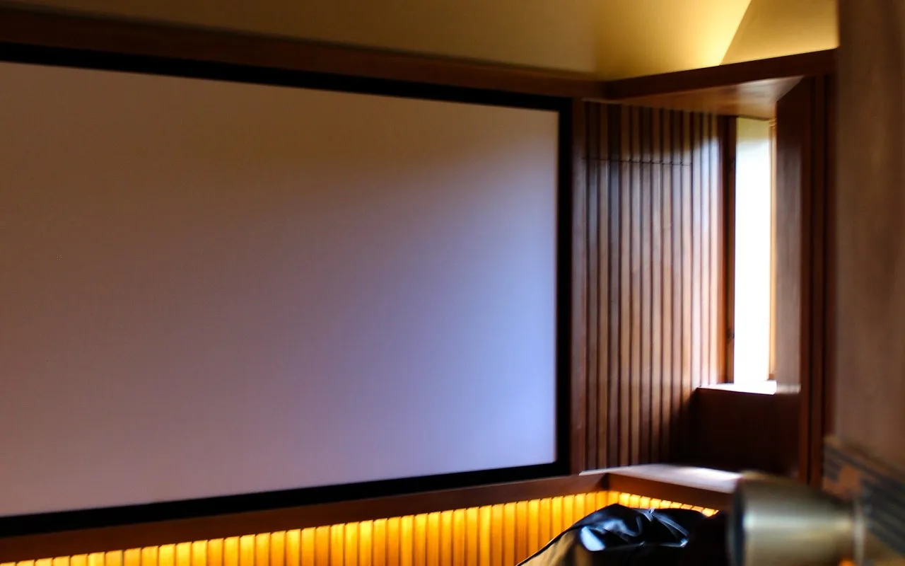 A loft home cinema with a wide screen set into a panelled gable, warm under-bench lighting and a projector on the eaves