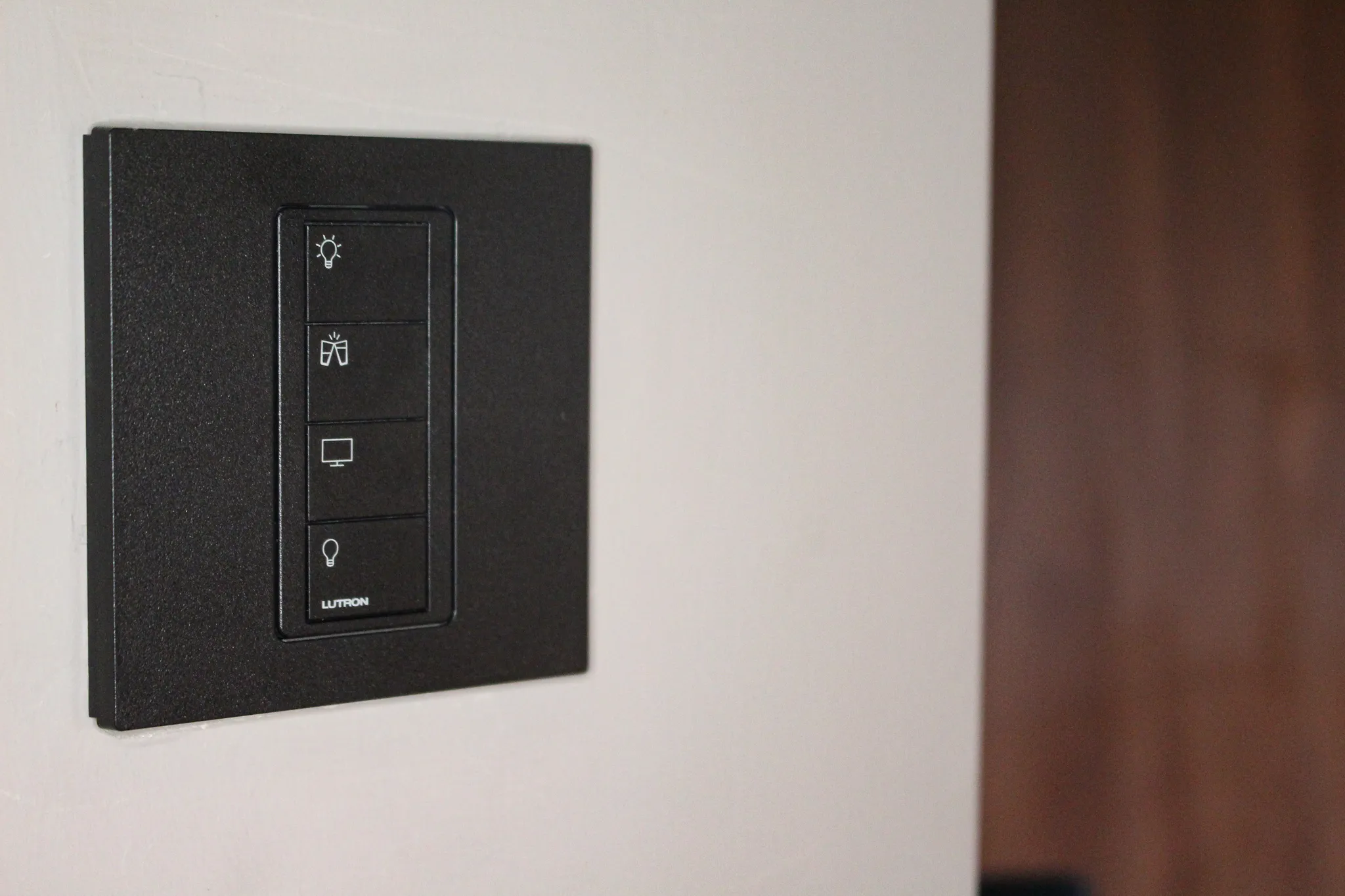 A black Lutron keypad on a pale wall, with icons for lighting, film and blinds