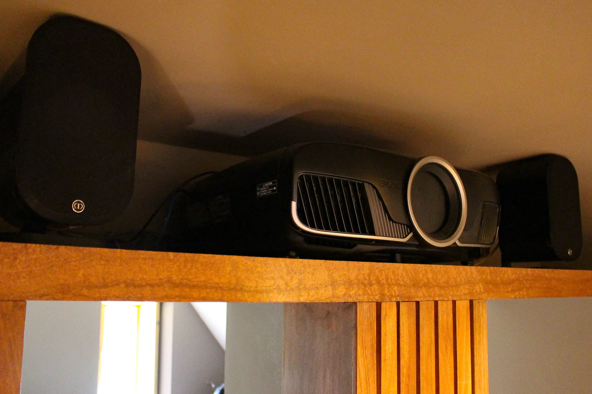 A home cinema projector and two surround speakers tucked onto a shelf in the eaves of a loft