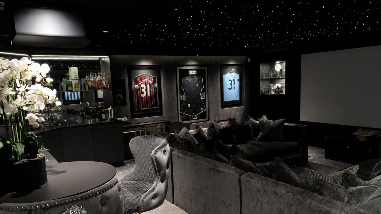 High-performance cinema lounge in black and charcoal with a starlight ceiling, a bar, framed football shirts and deep velvet seating