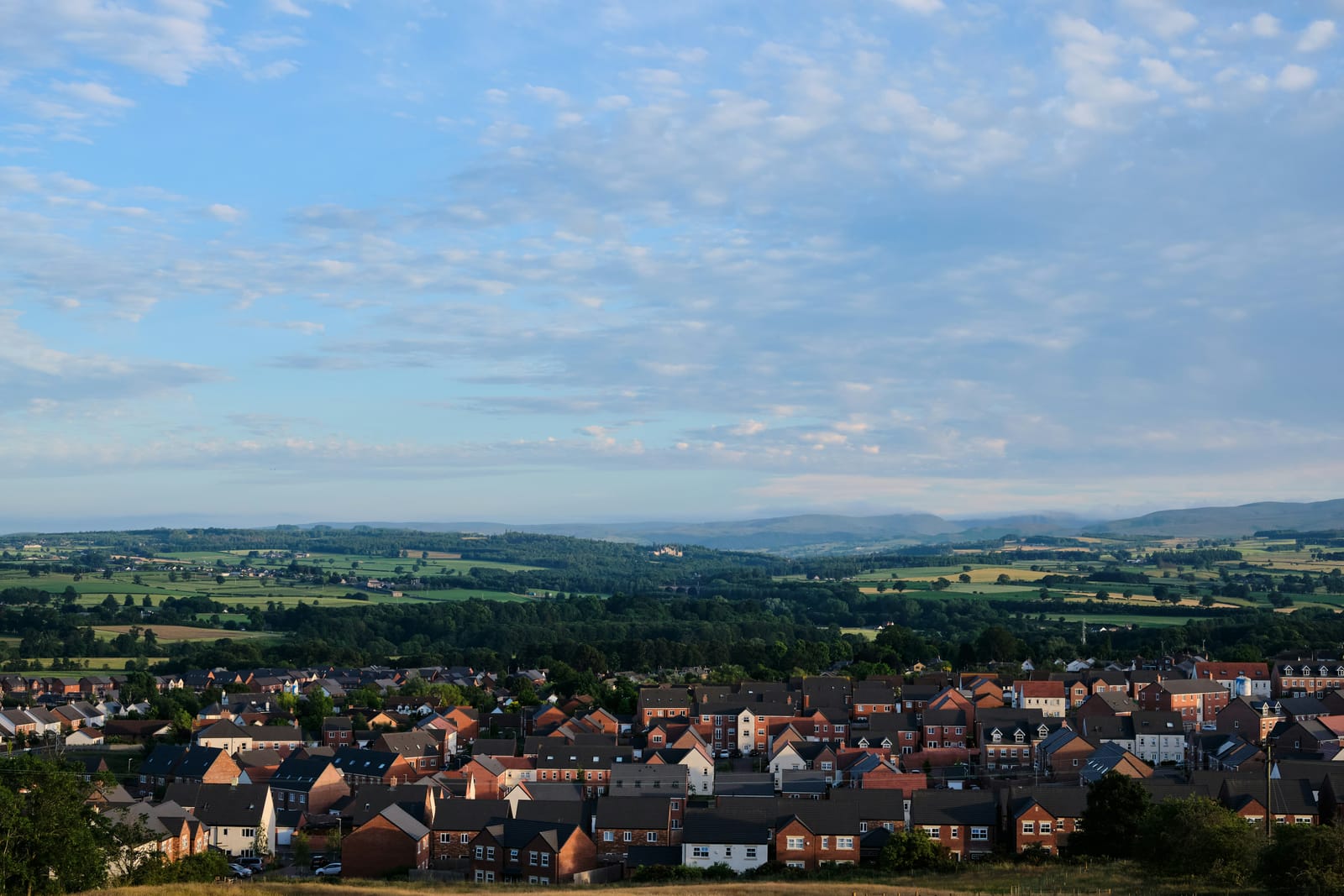 Modern houses on the edge of open farmland, with the fells rising in the distance