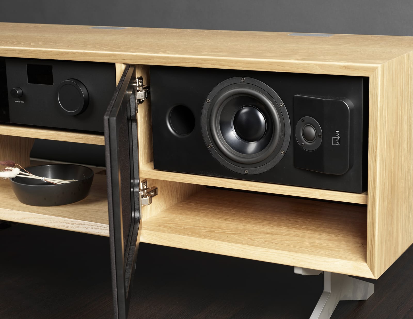 An oak media unit with its door open, showing an in-wall speaker and an amplifier built into the cabinetry