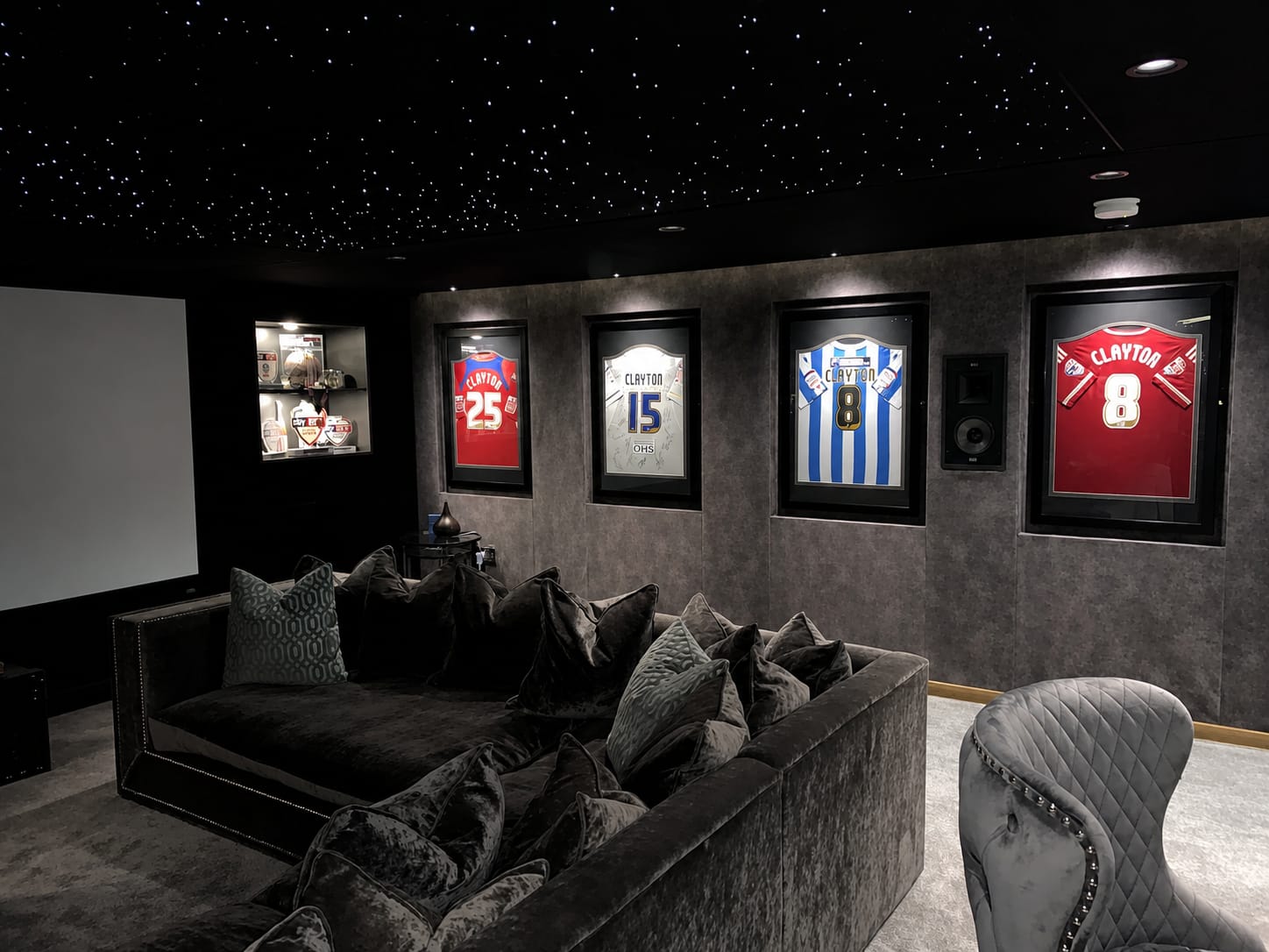 A cinema room with a fibre-optic starlight ceiling, grey fabric walls and a deep velvet corner sofa