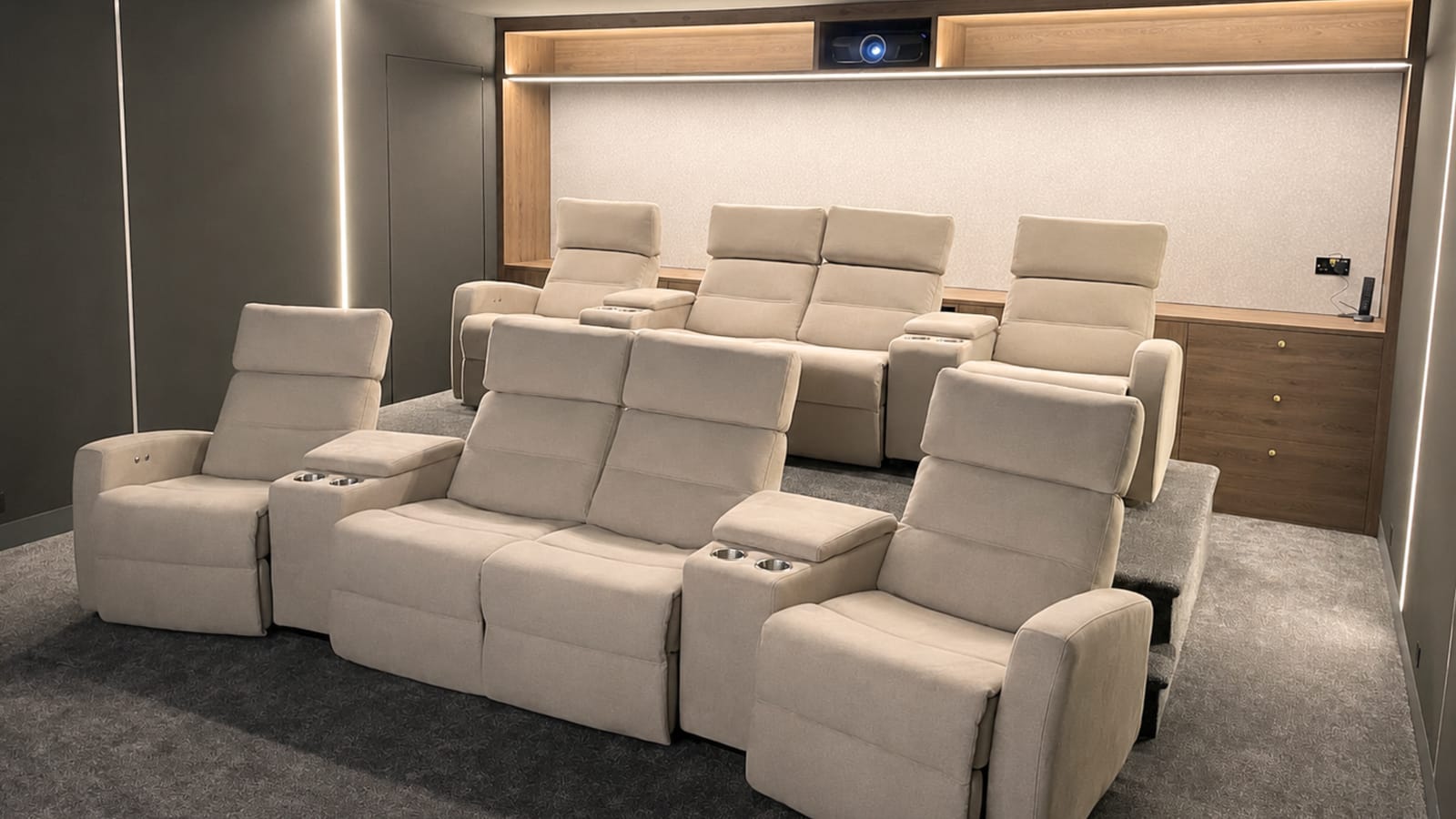 Two tiered rows of cream fabric recliners with cup holders in a home cinema, the rear row raised on a platform