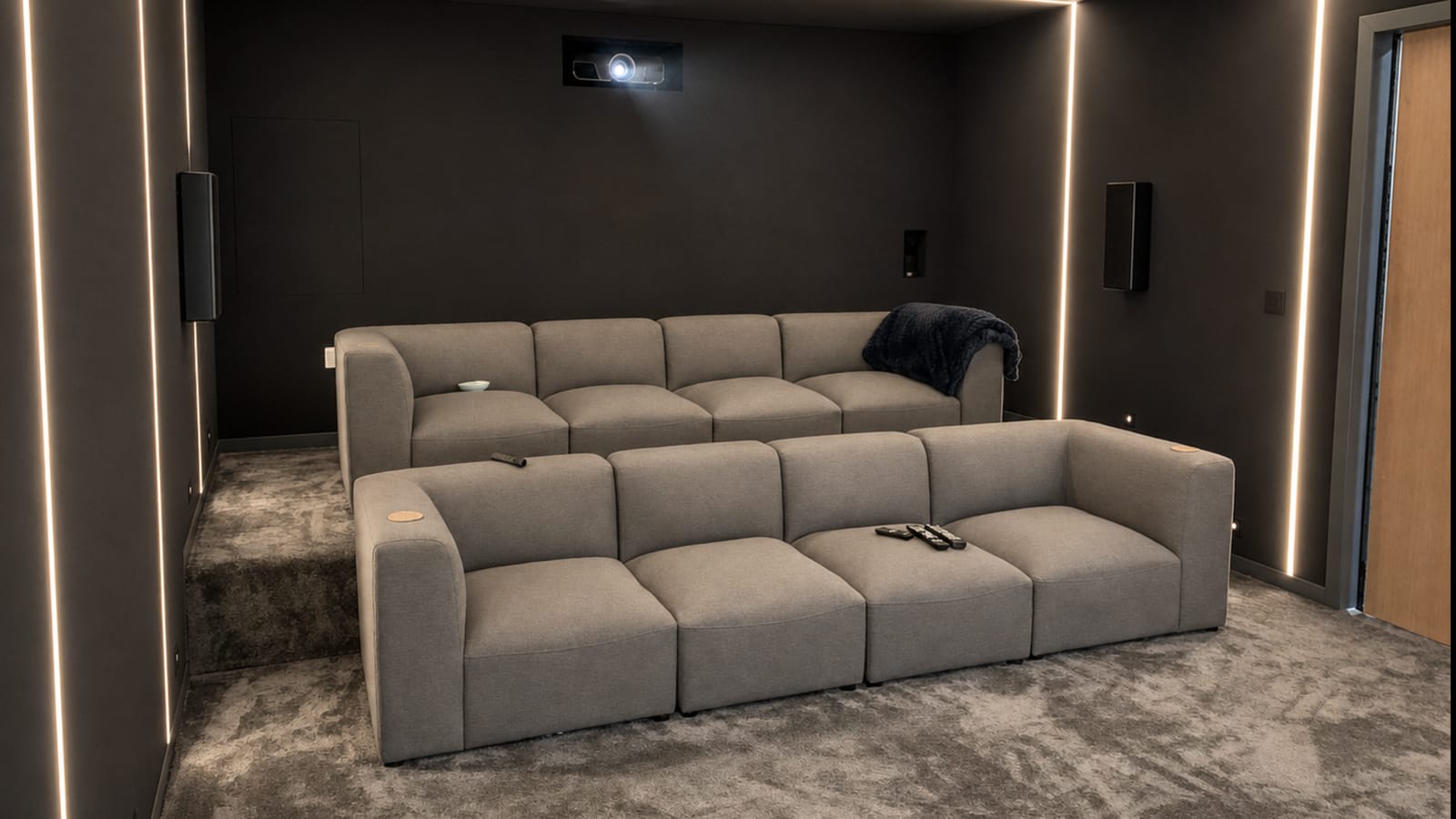 Two rows of modular grey fabric sofas in a dark cinema room, with vertical LED strips on the walls and a ceiling projector