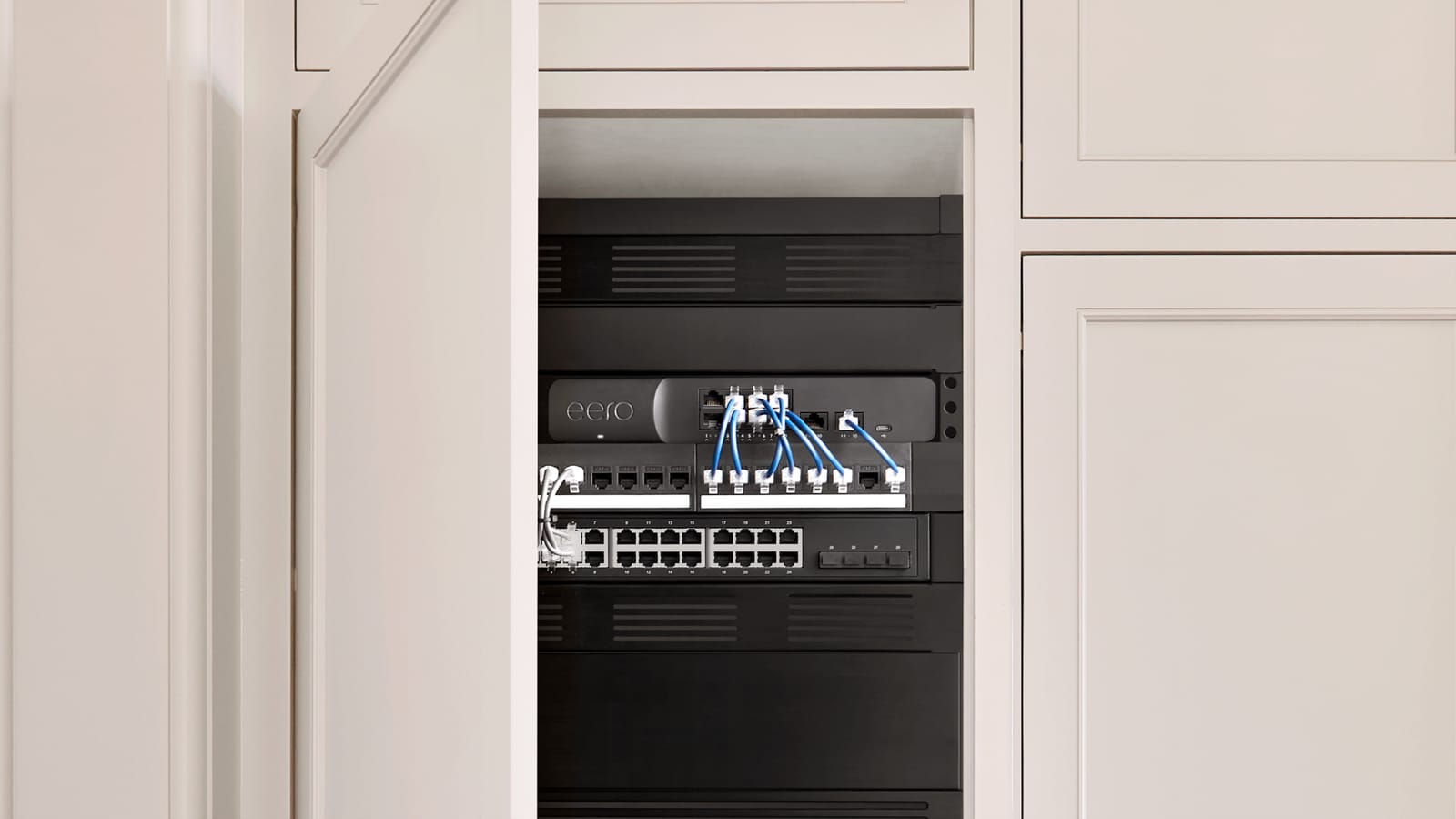 A network rack built into white joinery: a gateway, a patch panel and a 24-port switch with blue patch leads
